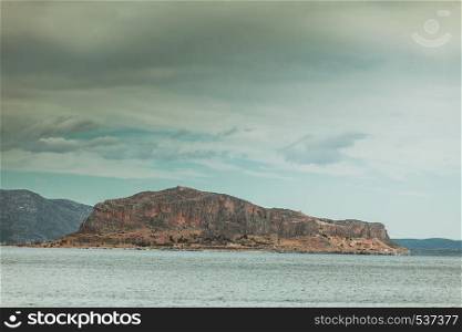 Greek island Monemvasia and cloudy sky, view from distance. Greece Peloponnese Lakonia. View of Monemvasia island in Greece