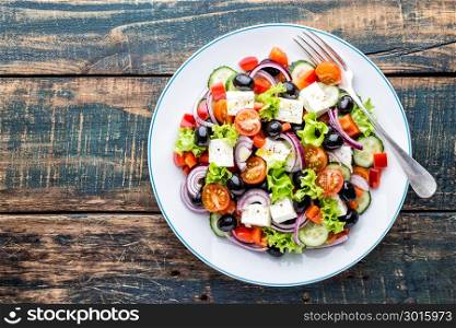 Greek salad of fresh cucumber, tomato, sweet pepper, lettuce, red onion, feta cheese and olives with olive oil. Healthy food, top view