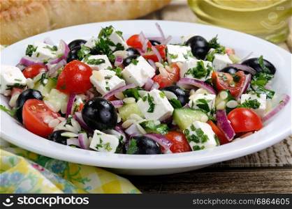 greek salad orzo pasta with black olive, red onion and cucumber, cherry tomatoes, feta and herbs. Horizontal shot. foreground
