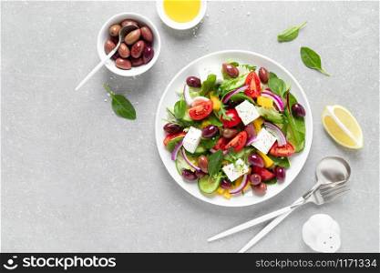 Greek salad with greens, olives and feta chesse on a white plate, top view