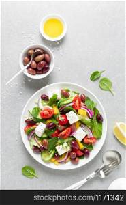 Greek salad with greens, olives and feta chesse on a white plate, top view