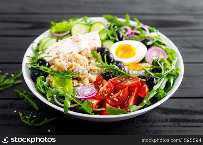 Greek style healthy breakfast bowl with oatmeal porridge and fresh vegetable salad of lettuce, arugula, olives, tomato, cucumber, feta cheese and boiled egg