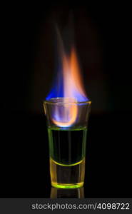 Green absinth drink on fire over black background