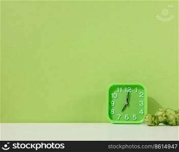Green alarm clock stands on a white table, green background. Back to school. Copy space