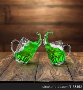 Green alcoholic drink splashes in the two bouncing beer mugs on a wooden table and blurred background. Happy St.Patrick &rsquo;s Day concept.. Fresh green beer splashes from two flying beer mugs.