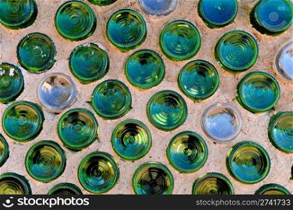Green and clear round glass bottles aligned geometrically in concrete. Alternative Building: Recycled Bottle Wall. . Commercial Photography