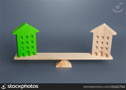 Green and ordinary houses are on the scales. Comparison of ecological housing with conventional housing. Advantages and disadvantages of energy efficient buildings. Net Zero Carbon emissions