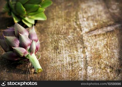 Green and purple artichokes on rustic wooden background .. Green and purple artichokes on rustic wooden background