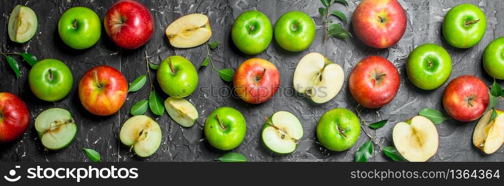 Green and red juicy apples with foliage and Apple slices. On black rustic background.. Green and red juicy apples with foliage and Apple slices.