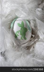 Green and white eggs on feather background. Easter conception with shape of rabbits on eggs.