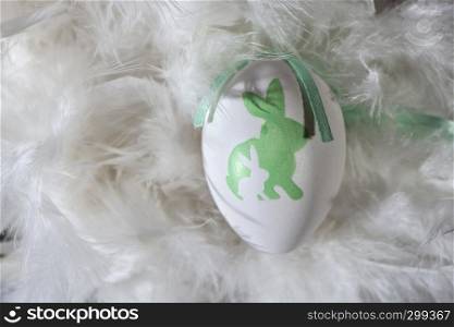 Green and white eggs on feather background. Easter conception with shape of rabbits on eggs.