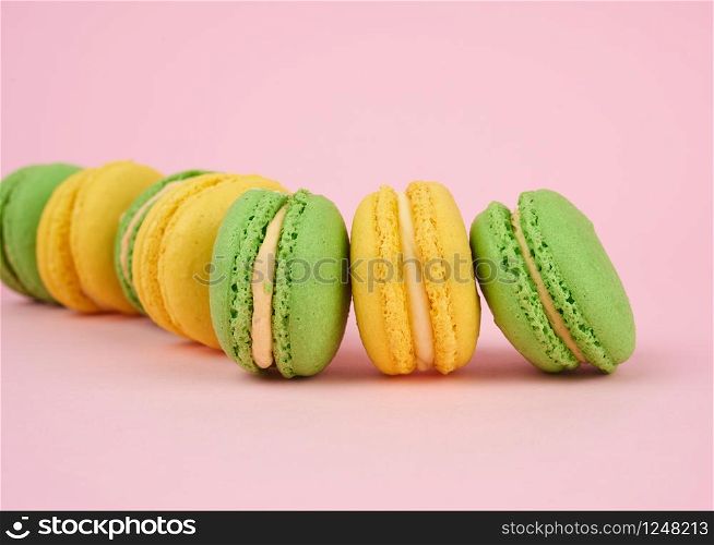 green and yellow round baked macarons on a pink background, delicious popular french dessert