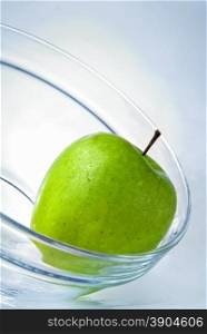 green apple in glass plate on blue background