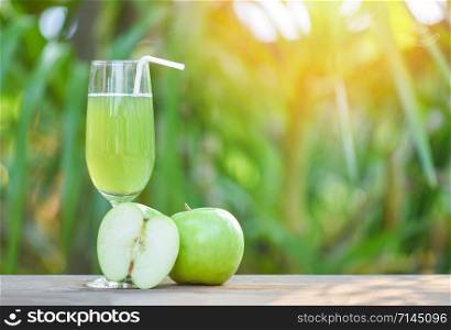 Green apple juice in glass and slice apple fruit with nature green summer background - selective focus