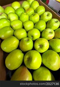 Green apples displayed in a cardboard box at the market.