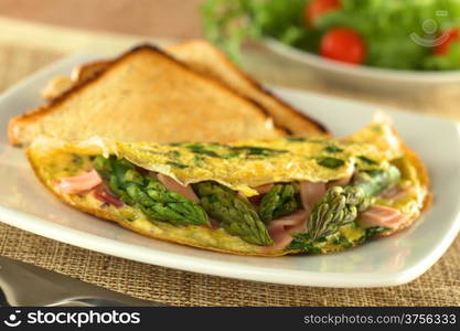 Green asparagus and ham omelet with toast bread and a fresh salad in the back (Selective Focus, Focus on the three asparagus tips in the front). Asparagus and Ham Omelet