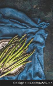 Green asparagus bunch on dark blue rustic background with kitchen towel, top view, place for text.