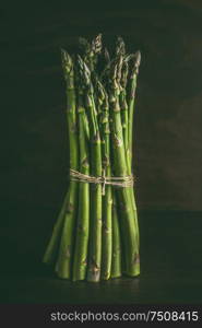 Green asparagus bunch standing on table at dark wall background. Spring seasonal vegetables.