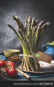 Green asparagus bunch with string and blank tag on dark rustic kitchen table with cooking ingredients