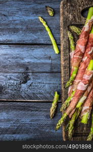 Green asparagus preparation with ham on dark gutting board, rustic blue wooden background, top view,frame