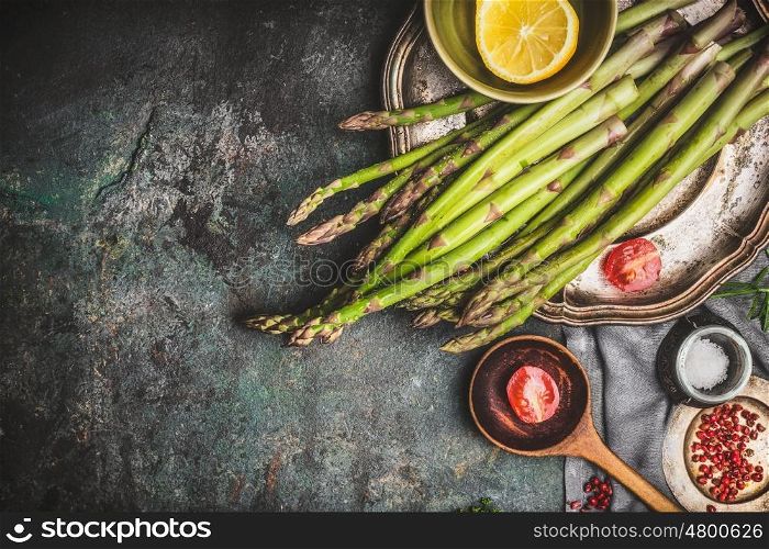 Green asparagus preparation with wooden cooking spoon and vegetables on rustic background, top view, border. Dark style