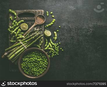 Green asparagus with edamame soybeans, lime and green peas on dark rustic kitchen table background, top view. Copy space. Healthy vegetarian food . Green cooking ingredients.