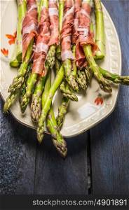 Green asparagus with parma ham in plate on rustic blue wooden background, close up