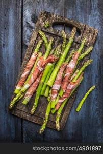 Green asparagus with parma ham on old gutting board, , rustic blue wooden background, top view