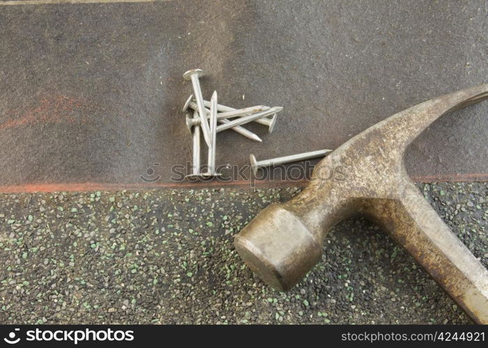 green asphalt shingle lined up on orange chalkline with roofing nails and worn hammer