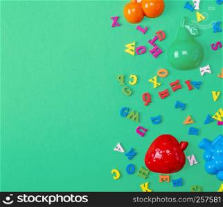 green background with childrens plastic toys and wooden multicolored letters, copy space