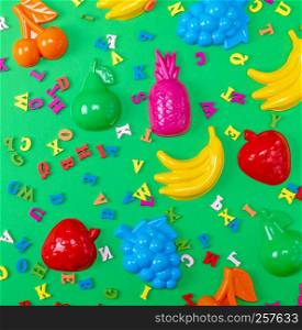 green background with childrens plastic toys and wooden multicolored letters, top view