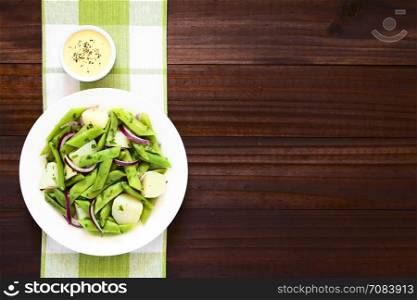 Green bean, potato and red onion salad with parsley, hollandaise sauce on the side, photographed overhead on dark wood with natural light