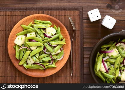 Green bean, potato and red onion salad with parsley served on wooden plate, photographed overhead on dark wood with natural light