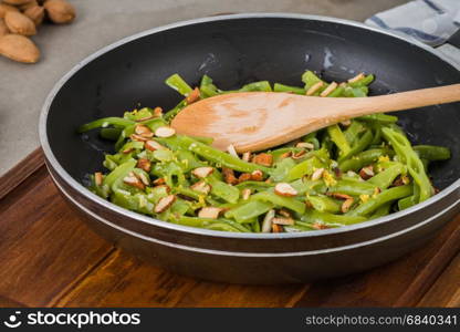 Green beans with roasted almonds on fry pan on kitchen countertop.