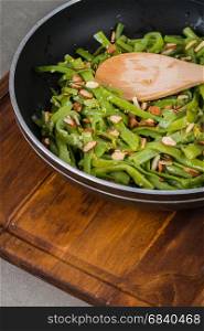 Green beans with roasted almonds on fry pan on kitchen countertop.