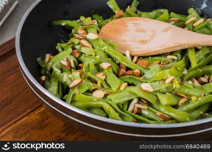 Green beans with roasted almonds on fry pan on kitchen countertop.