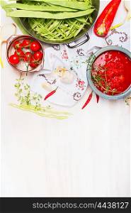 Green beans with tomatoes sauce, cooking preparation on light wooden background with traditionally embroidered cloth and ingredients, top view, place for text