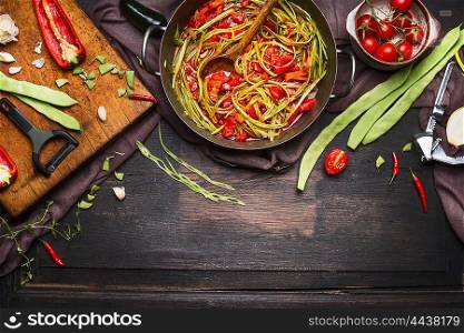 Green beans with tomatoes sauce in cooking pot with ingredients on cutting board for vegetarian dish on dark rustic wooden background, top view