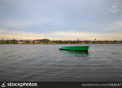 Green boat anchored in river Daugava with small town Plavinas in Latvia on the opposite bank on cloudy autumn day