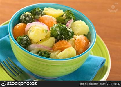 Green bowl full of fresh salad of potato, broccoli, mandarin and onion with mayonnaise (Selective Focus, Focus on the broccoli and the potato in the middle of the bowl)