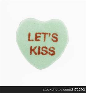 Green candy heart that reads lets kiss against white background.