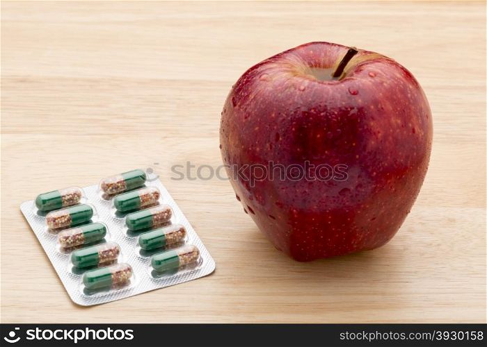 Green capsules bliter pack and fresh red apple . Green capsules bliter pack and fresh red apple on wooden background