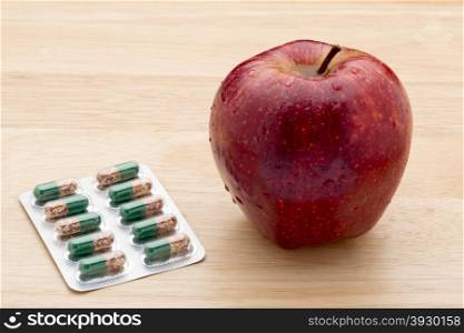 Green capsules bliter pack and fresh red apple . Green capsules bliter pack and fresh red apple on wooden background