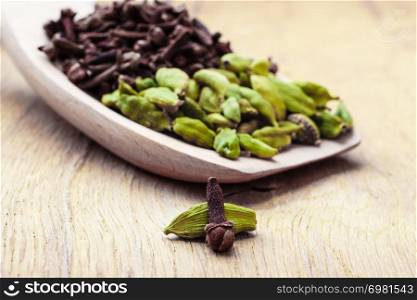 Green cardamom pods and cloves on wooden spoon rustic table background