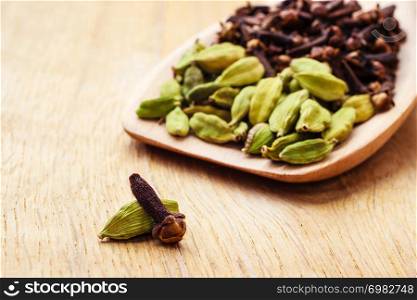 Green cardamom pods and cloves on wooden spoon rustic table background