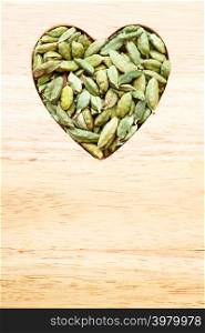 Green cardamom pods heap heart shaped on wooden rustic table background