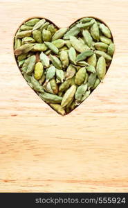 Green cardamom pods heap heart shaped on wooden rustic table background