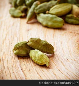 Green cardamom pods heap on wooden board background