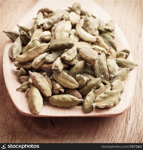 Green cardamom pods heap on wooden spoon rustic table background