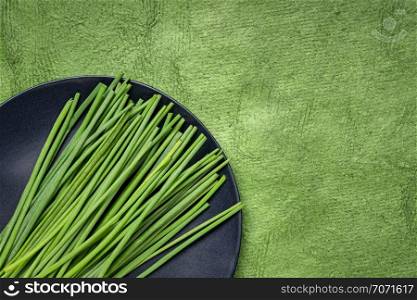 green chives on black plate against textured handmade bark paper with a copy space